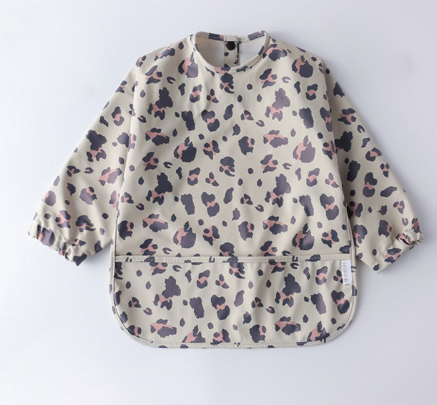 a child's bib with a pocket in the lower front part. The color is light dirty green with leopard prints on it