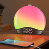 a sunrise light alarm clock laying on the bed with a phone in front of it. The clock displays time and warm light like a sunlight